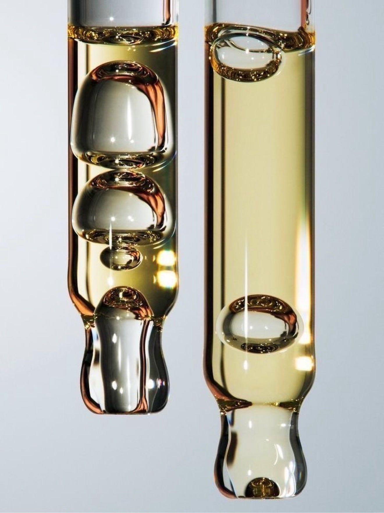 Glass pipettes of golden MelaBODY Nourishing Glow Oil with bubbles suspended inside