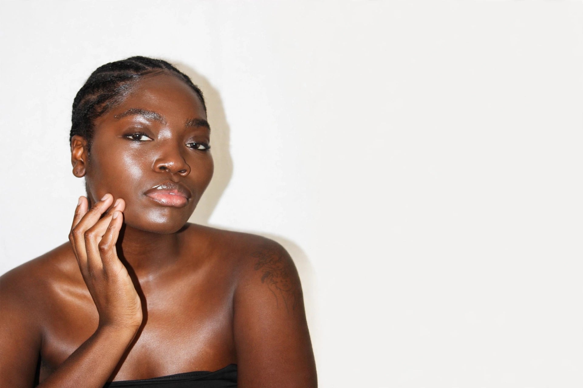 Woman with braids and rich brown, glowing skin resting her hand along her jaw
